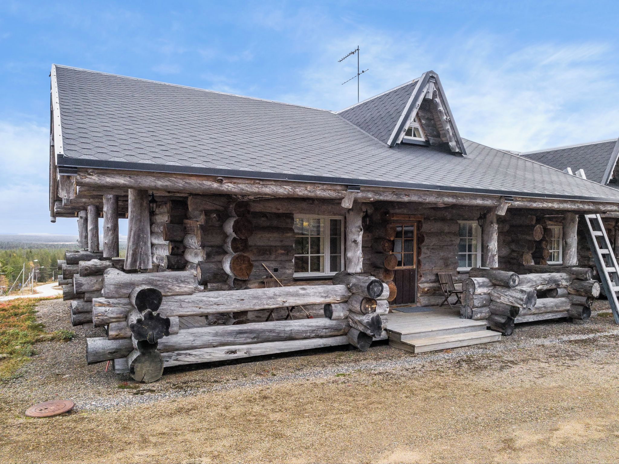 A log cabin with a steeply pitched roof, a front porch with steps, and a chimney.