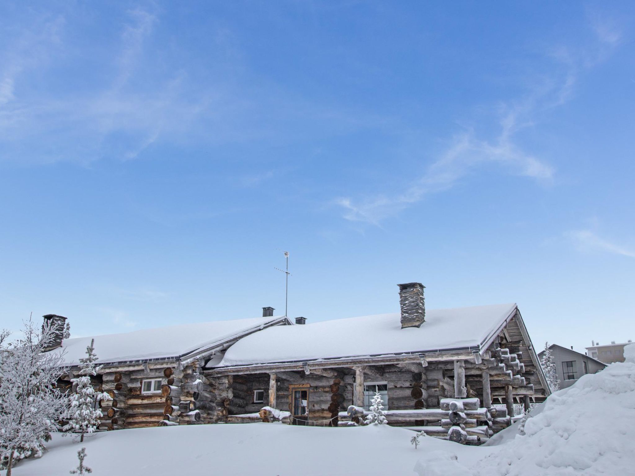 Une cabane en rondins avec un toit enneigé, une cheminée et un petit porche.