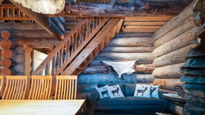 Ein Blockhaushaus-Interieur mit einer Holztreppe, einem Esstisch, einer Couch mit Tier-Kissen und einem rustikalen Holzboden.