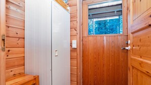 A wooden cabin with a white refrigerator, a wooden bench, and a door with a window.