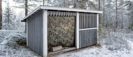 A small, wooden cabin with a sloped roof, surrounded by a snowy forest.