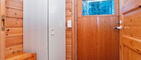 Een houten interieur met een witte deur, een klein houten bankje en een raam met uitzicht op bomen.