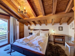 Une chambre avec un plafond en bois, un lit avec une literie blanche, une table de chevet, un bureau et une chaise.