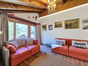 A cozy living room with two red sofas, a chandelier, and framed pictures on the wall. - Haus Rollin by Interhome (Zermatt)