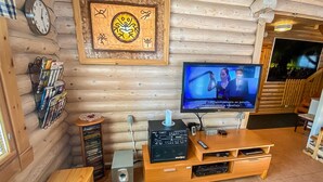 L’intérieur chaleureux d’un chalet en rondins est agrémenté d’un meuble de rangement en bois servant de centre de divertissement, d’un téléviseur à écran plat et d’une horloge murale.