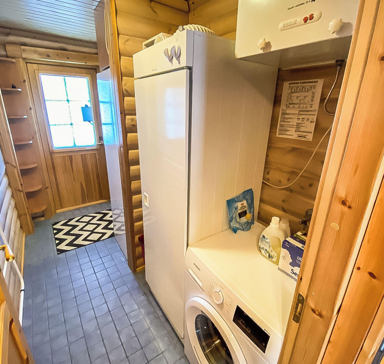 Un baño pequeño con lavadora, refrigerador y ventana con persianas.