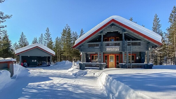 Un hôtel aménagé dans un chalet en rondins, à l’extérieur rouge et blanc, entouré de neige et d’arbres.