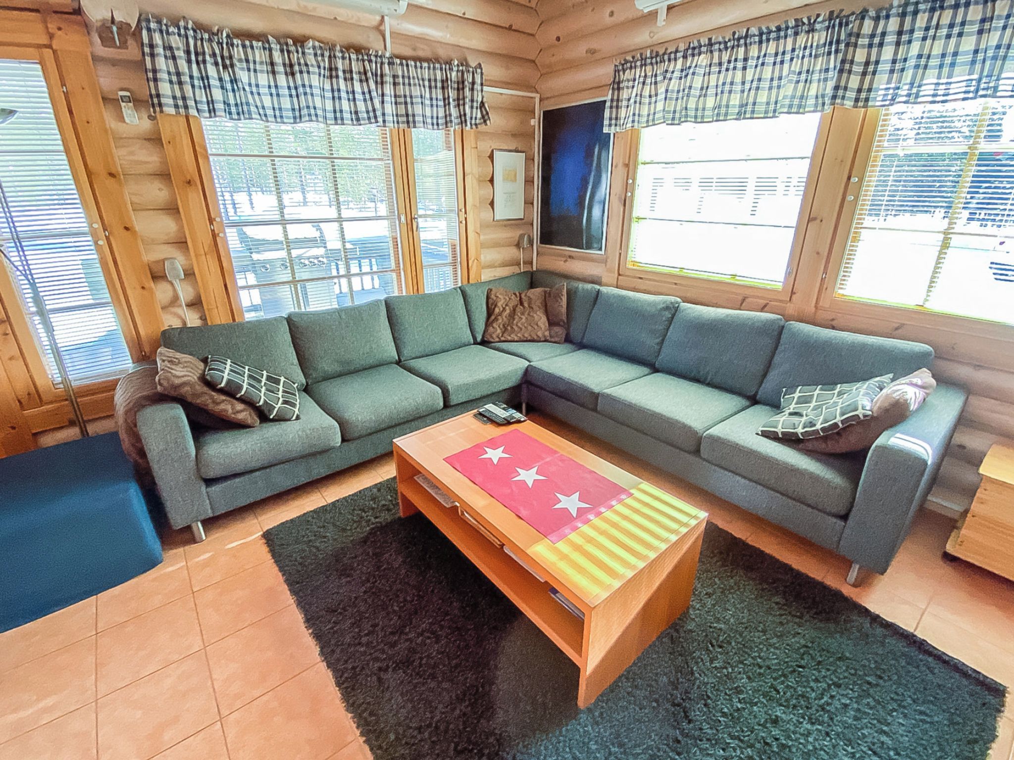 A cozy living room with a sectional sofa, a wooden coffee table, and large windows with curtains.