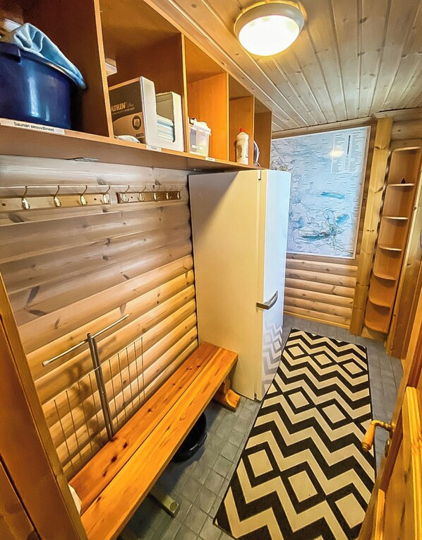 A compact room with a bench, a white refrigerator, and a wooden bench with a metal backrest.