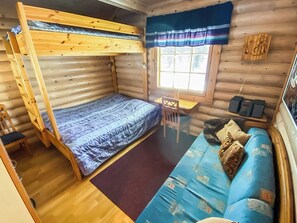 A compact cabin with a bunk bed, a small desk, a sofa, and a window with curtains.