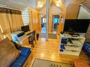 Een houten vloer, een bank, een bureau met een computer, een televisie en een boekenkast in de inrichting van een vakantiehuisje.