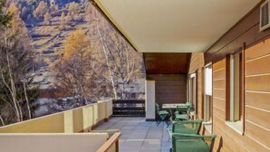 A balcony with a table and chairs, overlooking a mountainous landscape.