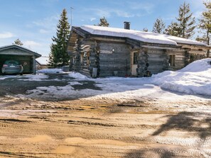 A log cabin with a snow-covered roof, a garage, and a dirt driveway.