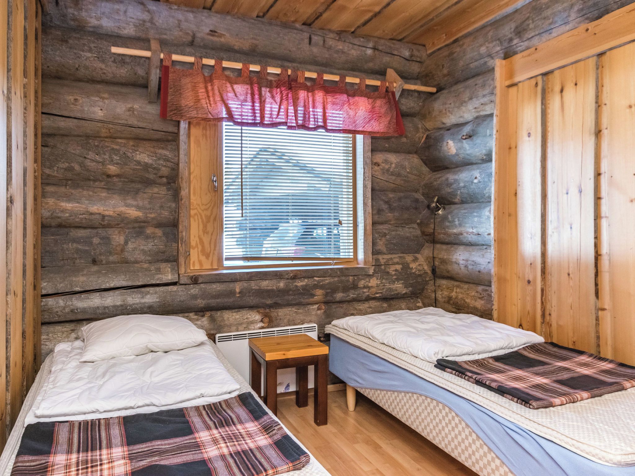 Eine Hütte mit zwei Betten, einem kleinen Tisch und einem Fenster mit Jalousien.