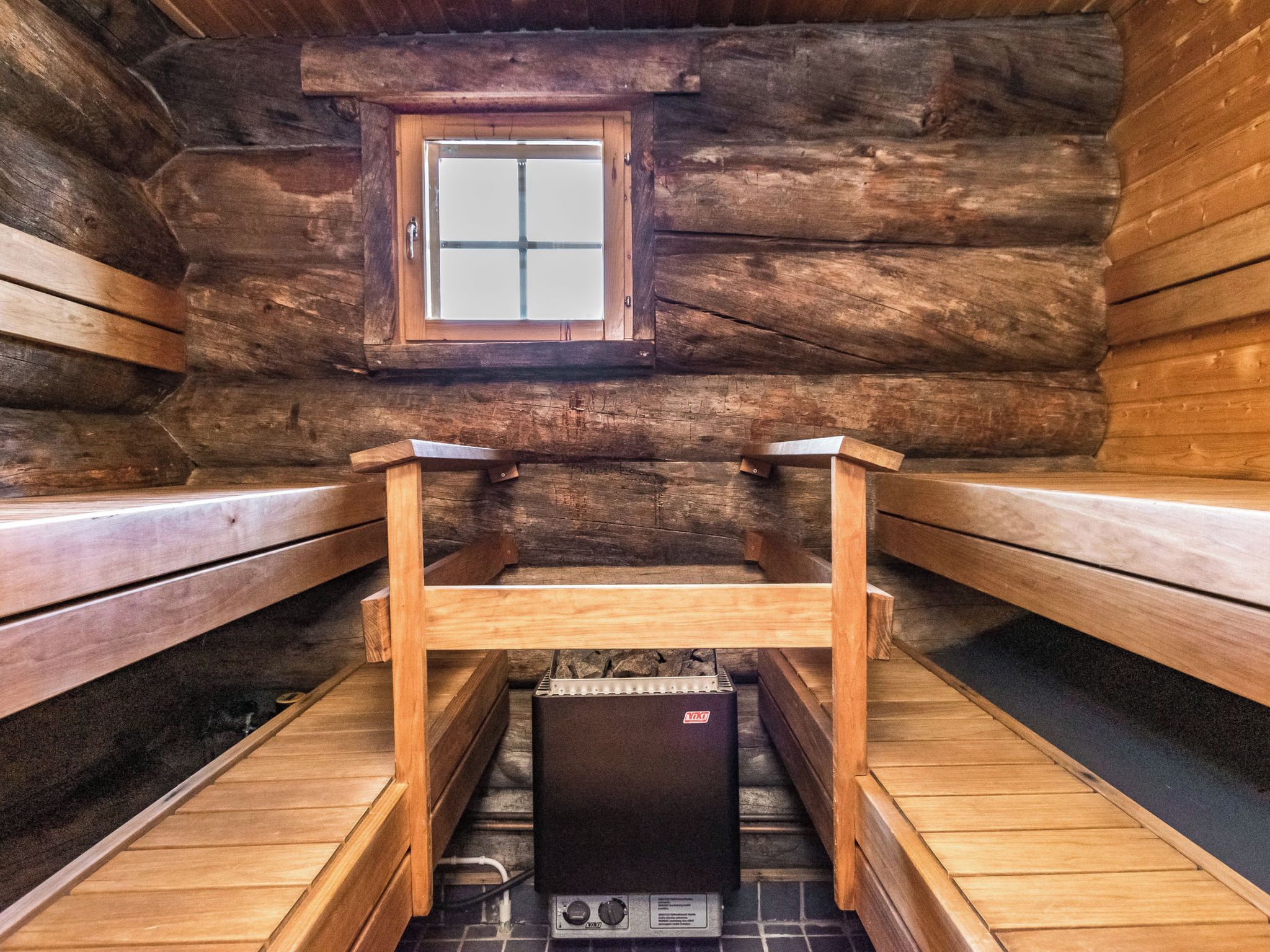 Un sauna avec des bancs en bois, une fenêtre et un appareil de chauffage pour sauna.