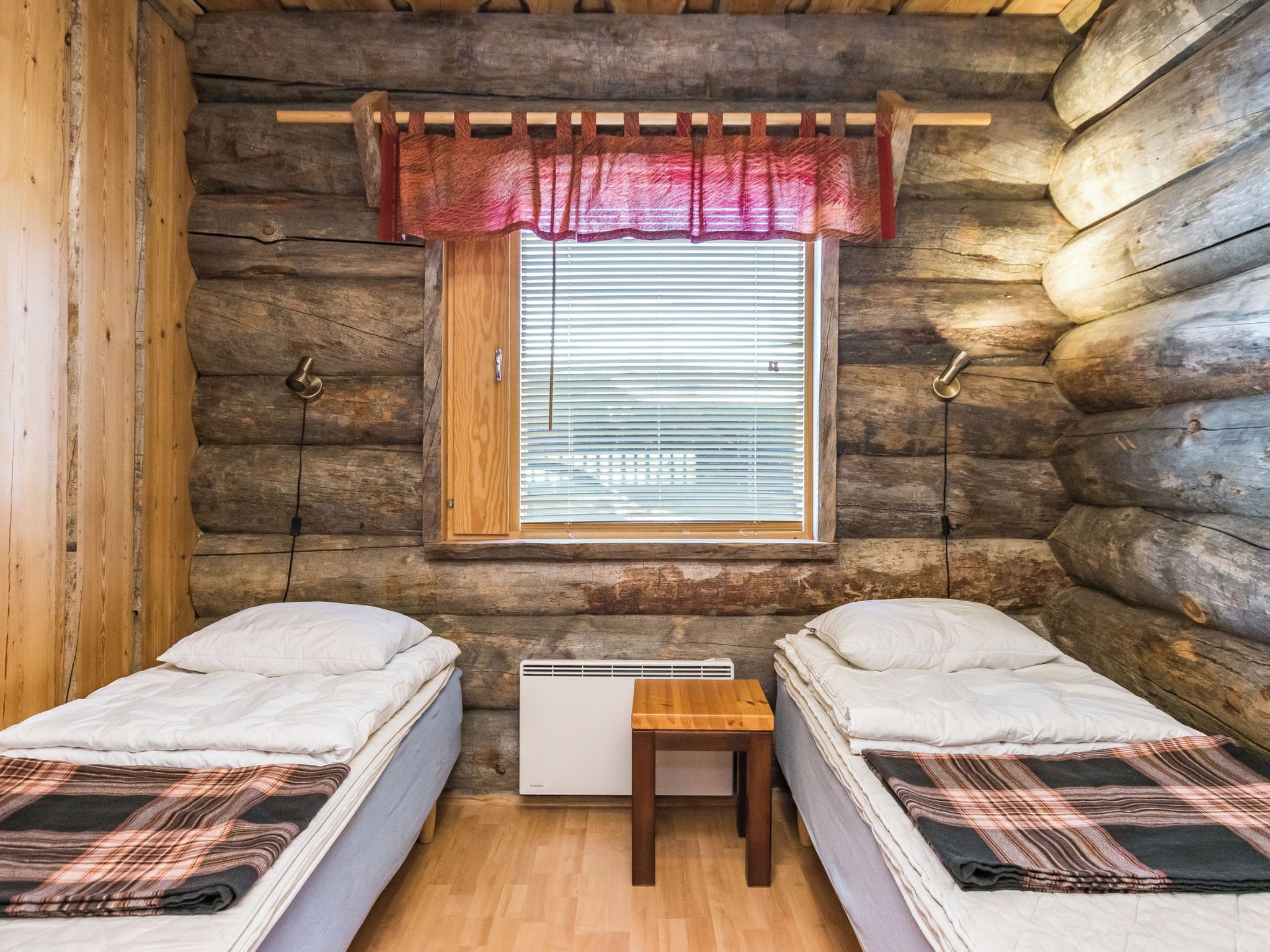 Une chambre de style rustique avec deux lits, une fenêtre avec des stores, un radiateur et une petite table.