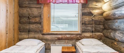 A log cabin room with two beds, a window with blinds, a heater, and a small table.