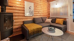 L’intérieur d’un chalet confortable, avec des murs en bois, un canapé, une table, une cheminée et une fenêtre équipée de stores.