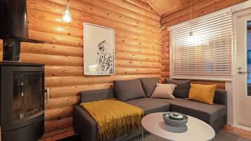 A cozy cabin interior with a sofa, a table, a fireplace, and a window with blinds.
