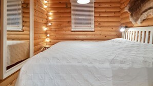 Une chambre confortable dans un chalet en rondins, avec un grand lit, des murs en bois et un luminaire au plafond.