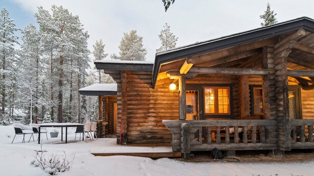 Une cabane en rondins dotée d’un porche couvert et d’un coin repas, entourée d’arbres recouverts de neige.