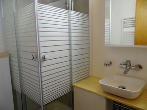 Ein Badezimmer mit Duschkabine aus Glas, einem weißen Waschbecken und einem Spiegel darüber.