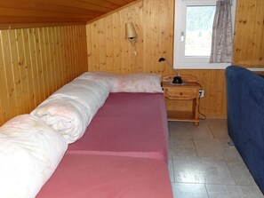 Ein Einzelbett mit rosa Matratze und Holz Kopfteil in einem Zimmer mit Holzwänden und einem Fenster.