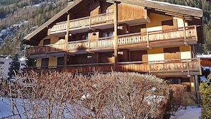 Un chalet in legno a più piani con balconi, sullo sfondo di montagne innevate.