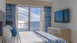 A hotel room with a bed, a TV, a dresser, and a view of the ocean. - 2BR/2BA Condo: Beachfront, Pool & Balcony (Treasure Island)