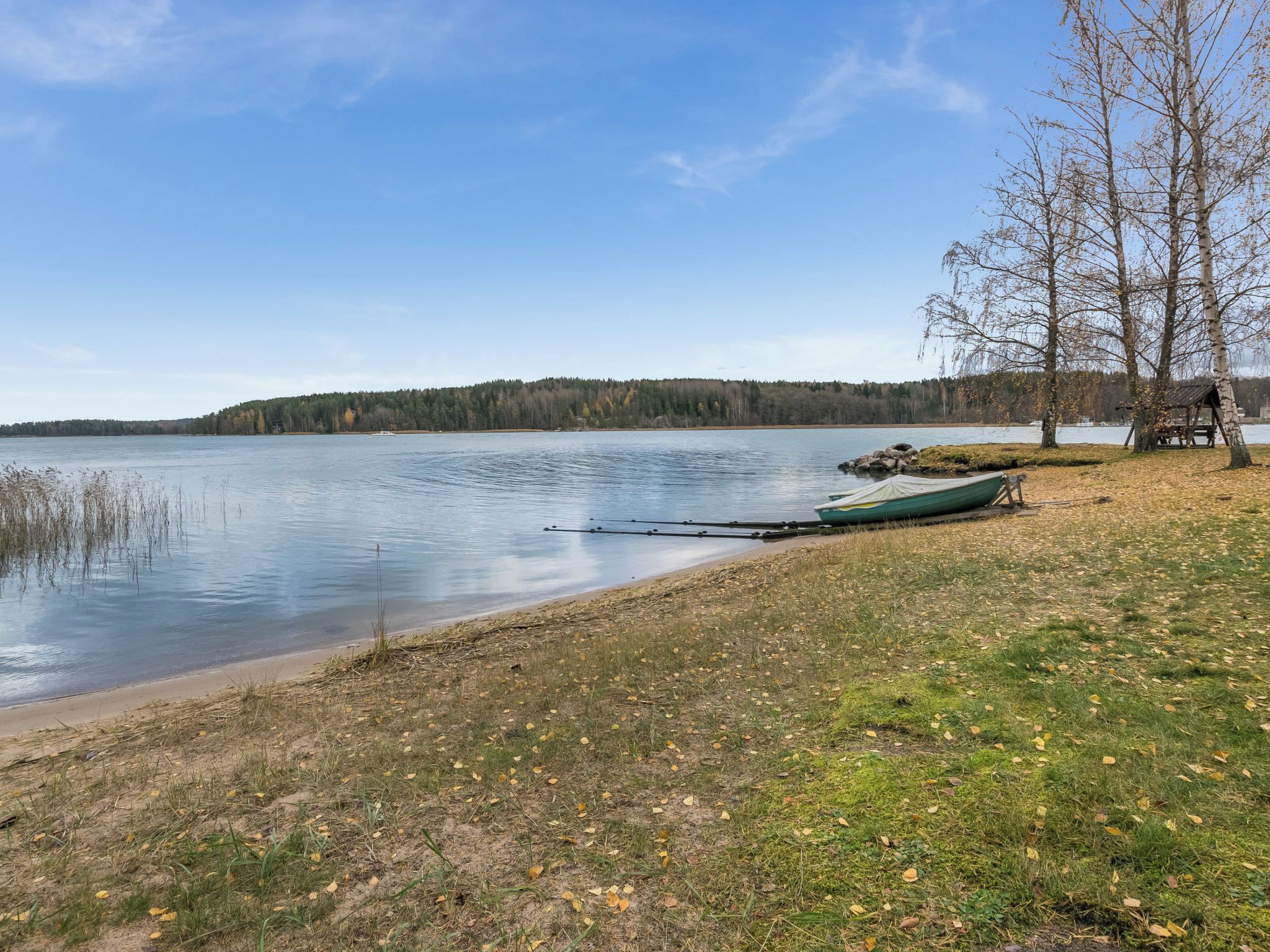 Vista de un lago con un muelle, una pequeña estructura de madera y una colina boscosa al fondo.