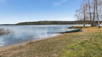 Vista de un lago con un muelle, una pequeña estructura de madera y una colina boscosa al fondo.