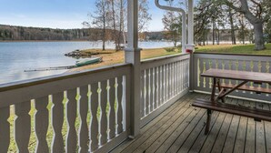 Um deck de madeira com guarda-corpo, mesa de piquenique e vista para um lago e árvores.