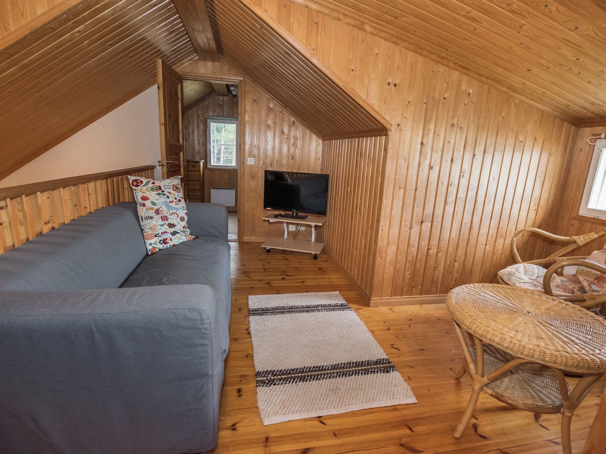 Une pièce confortable de style loft, avec un canapé, un téléviseur, un fauteuil en osier et un petit tapis sur le plancher en bois.
