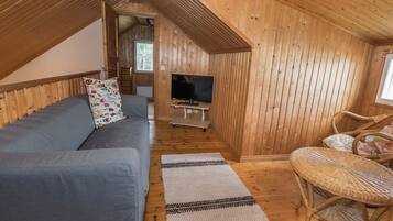 A cozy loft-style room with a sofa, a television, a wicker chair, and a small rug on the wooden floor.