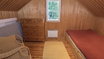 Un pequeño dormitorio en ático con paredes de madera, una ventana, un aparador, una cama y una cesta tejida.