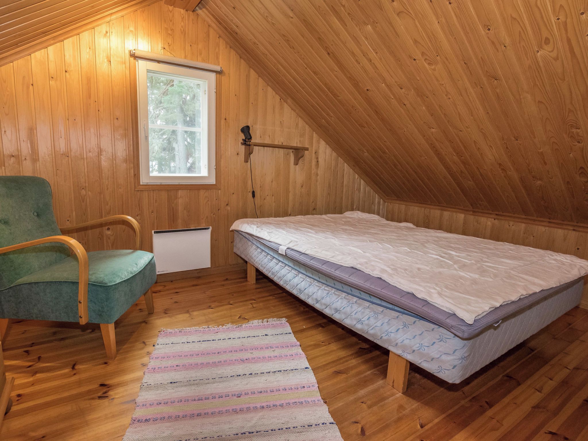 A small, sloped-roofed room with wooden walls, a single bed, a chair, and a window.