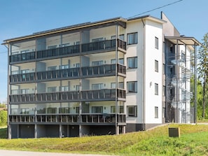 Un edificio residencial de varios pisos con balcones, una escalera de incendios y un paisaje verde.