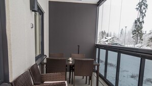 A balcony with wicker furniture, a table, and a view of a snowy landscape.