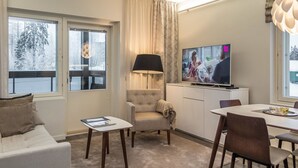 A modern hotel room with a sofa, armchair, dining table, and TV.