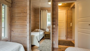 Una habitación tipo cabaña de madera con dos camas, una puerta corredera y una mesita de noche pequeña con una lámpara.