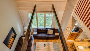 Un moderno espacio tipo loft con piso de madera, un sofá de color marrón oscuro, una mesa de centro de madera y un comedor con mesa y sillas de madera.