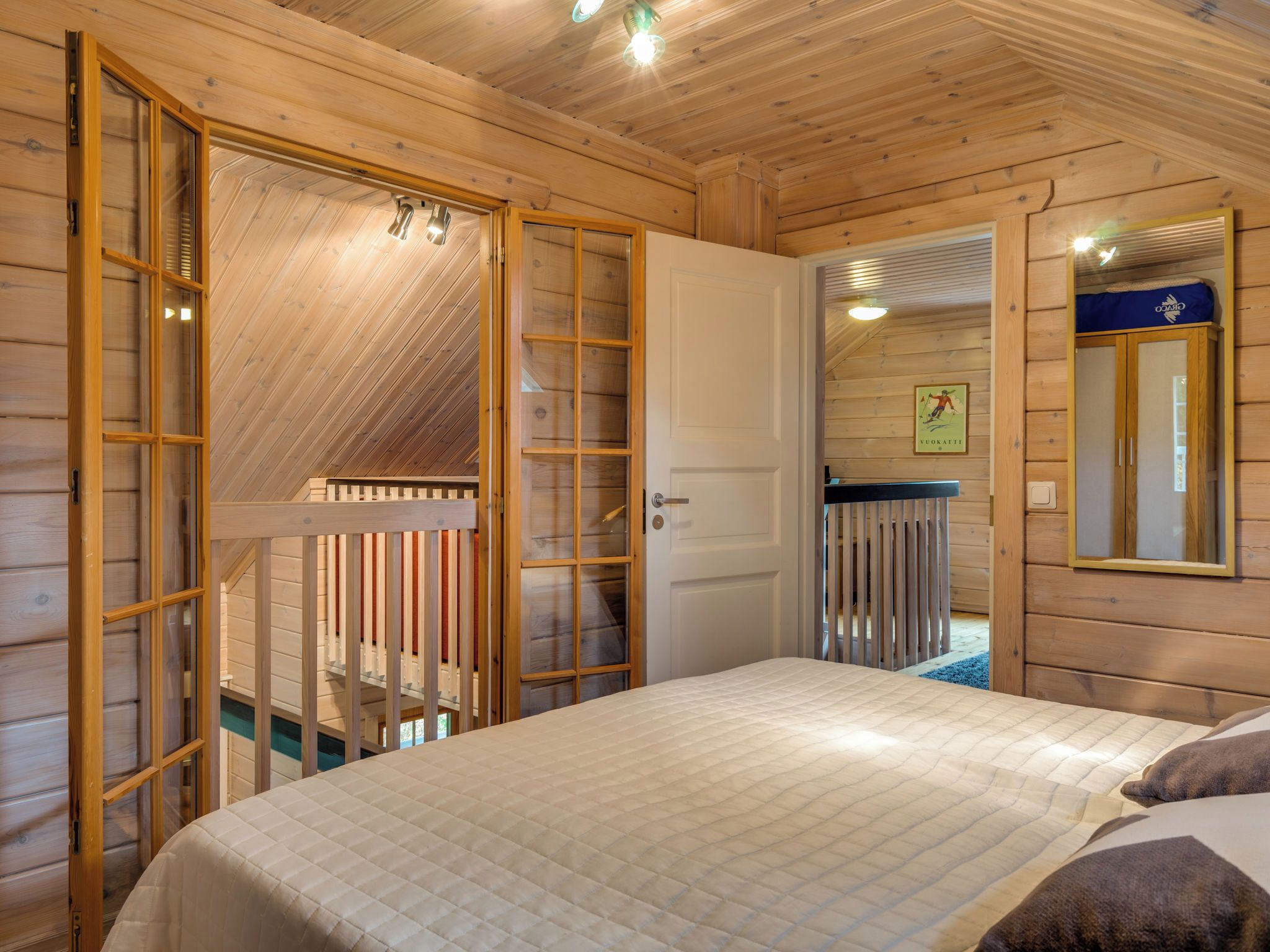 A wooden room with a bed, a door leading to a balcony, and a mirror on the wall.