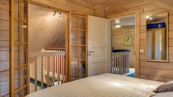 A wooden room with a bed, a door leading to a balcony, and a mirror on the wall.
