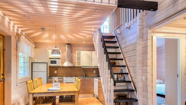 Una cocina moderna con armarios de madera, un comedor con mesa y sillas de madera, y una escalera con barandal negro.