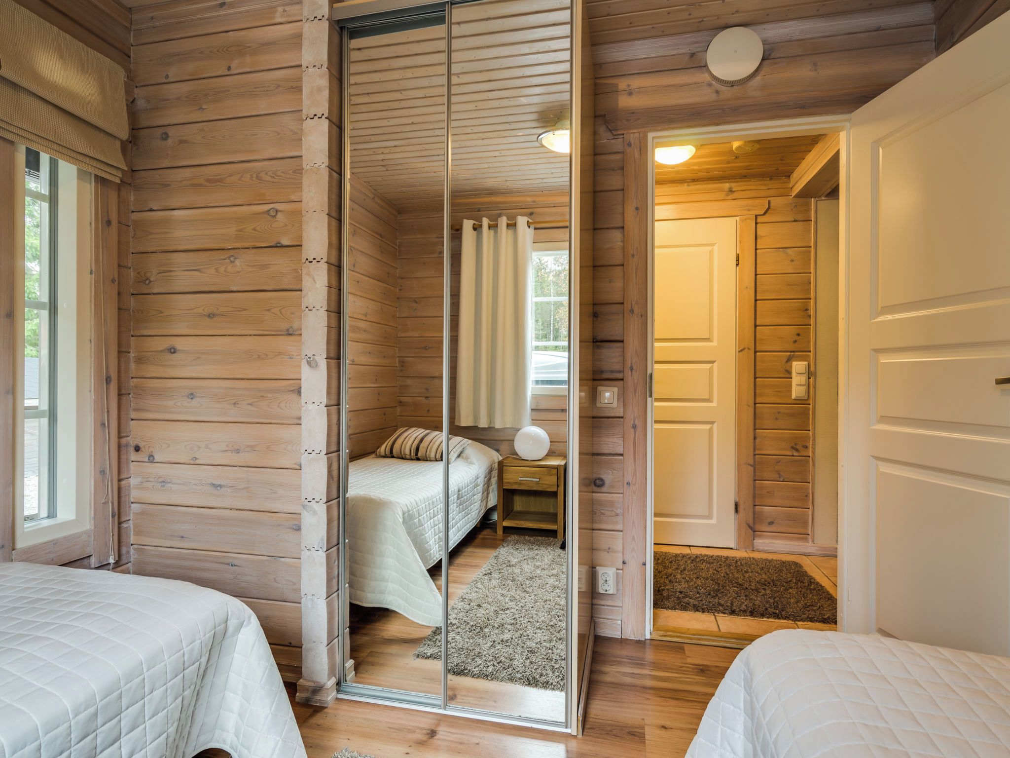 Un dormitorio tipo cabaña de madera con dos camas, un espejo y una puerta que da a otra habitación.