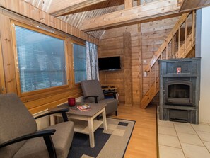 A cozy cabin interior with a wooden interior, a television mounted on the wall, a fireplace, and a staircase leading to an upper level. - Rukannaava 1a (2) by Interhome (Kuusamo)
