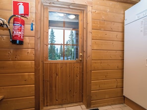 A wooden door with a window, a fire extinguisher mounted on the wall, and a refrigerator to the right.