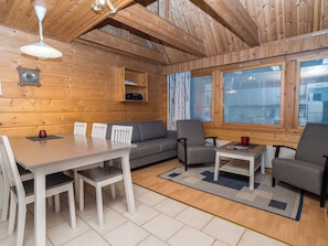 A wooden interior with a dining table, chairs, a sofa, and two armchairs.