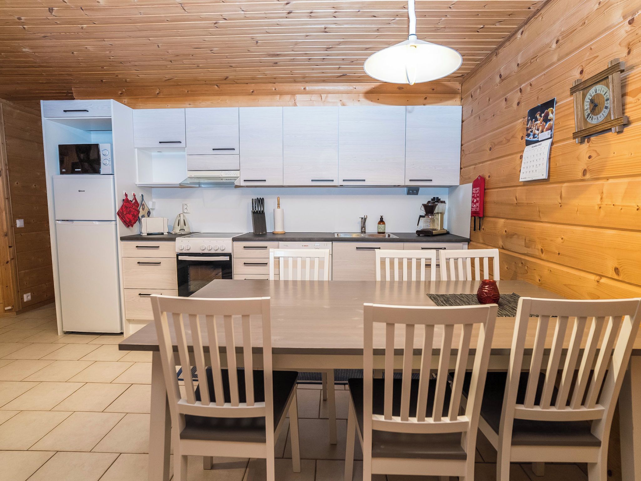 A modern kitchen with white cabinets, a built-in oven, and a dining area with a table and chairs.