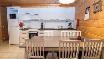 A modern kitchen with white cabinets, a built-in oven, and a dining area with a table and chairs.